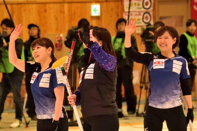観客に手を振る三人のカーリングの選手