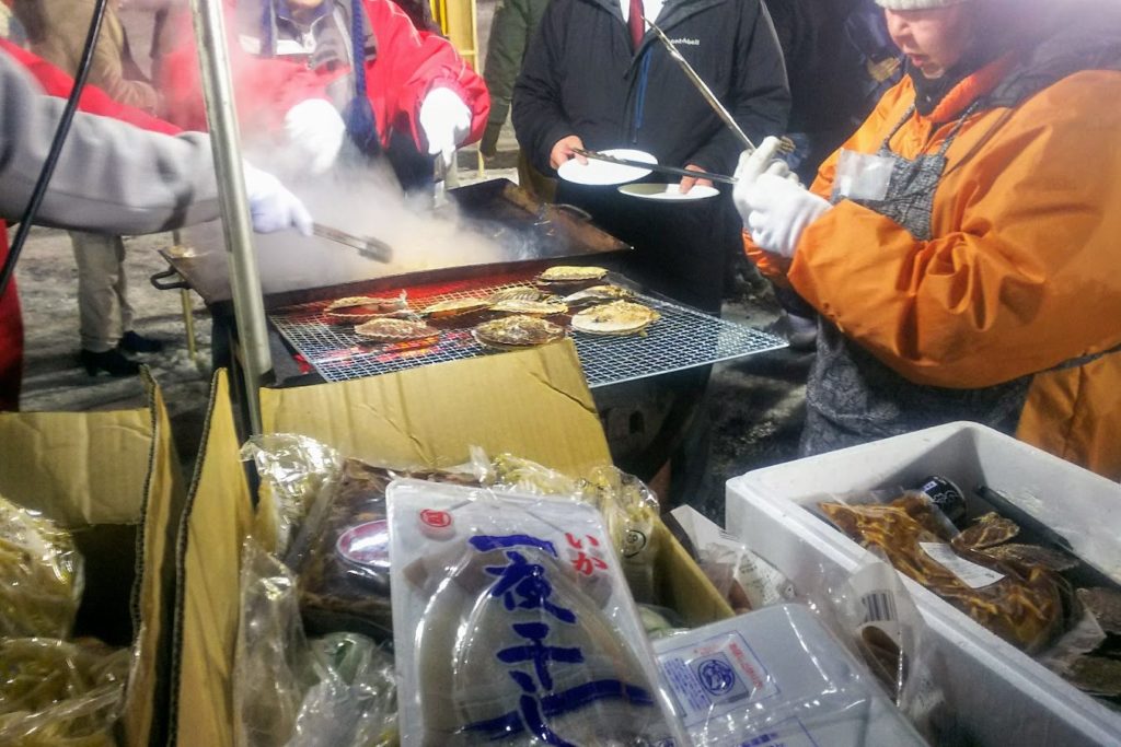 ストーブで焼かれる帆立を食べる人々