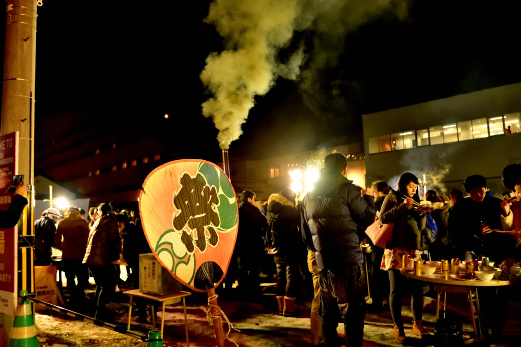 夜の屋台に集まる人々と大きなうちわ